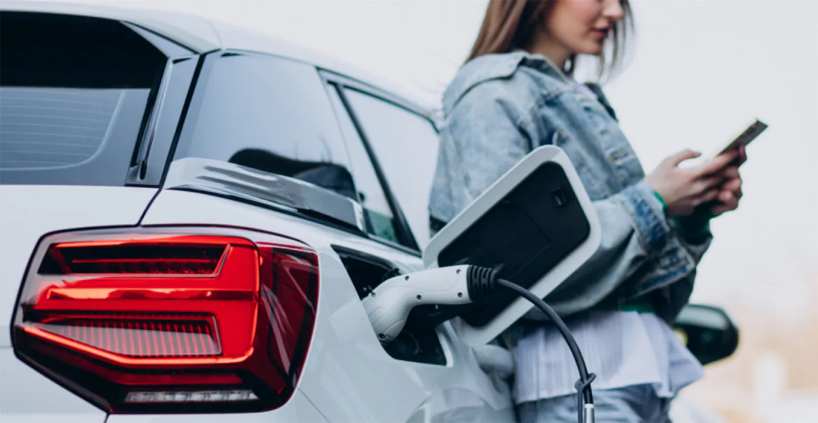 Woman standing beside an electric car charging, highlighting the application of Lemon Law to electric vehicles in California