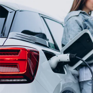 Woman standing beside an electric car charging, highlighting the application of Lemon Law to electric vehicles in California